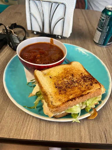 Toasted sandwich on a teal plate served with a bowl of chili
